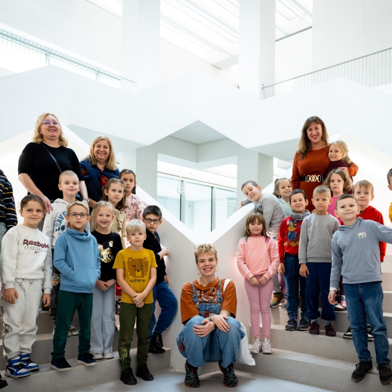 Zdjęcie. Klasa szkola pozuje do zdjęcia na tle białej klatki schodowej Muzeum Sztuki Nowoczesnej w Warszawie. 