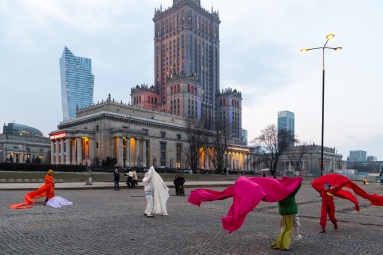 Osoby performerskie w kolorowych kostiumach na placu Defilad. 